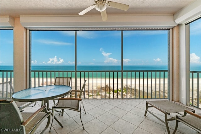 sunroom with a water view, a beach view, and ceiling fan