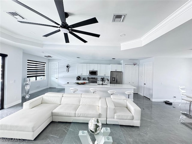 living room featuring ceiling fan, a tray ceiling, crown molding, and sink