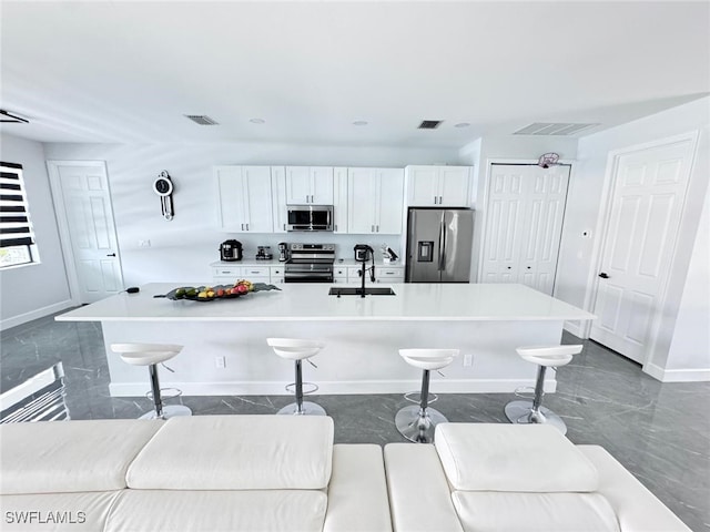 kitchen with white cabinets, an island with sink, sink, stainless steel appliances, and a breakfast bar