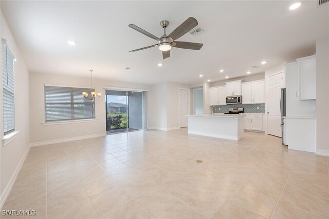 kitchen featuring white cabinetry, hanging light fixtures, decorative backsplash, a center island with sink, and appliances with stainless steel finishes