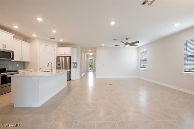 kitchen featuring a center island with sink, white cabinets, ceiling fan, light tile patterned floors, and appliances with stainless steel finishes