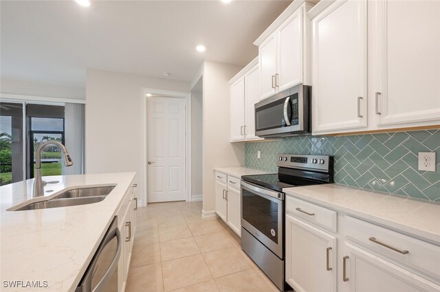 kitchen featuring white cabinetry, sink, stainless steel appliances, tasteful backsplash, and light stone counters