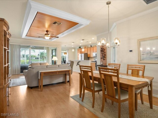 dining area featuring ceiling fan with notable chandelier, visible vents, ornamental molding, light wood finished floors, and a raised ceiling