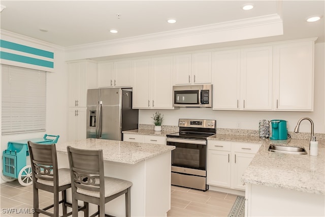 kitchen featuring a breakfast bar, white cabinets, light stone countertops, stainless steel appliances, and sink