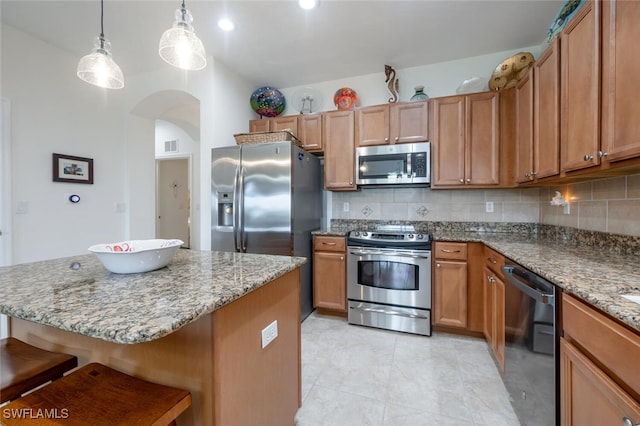 kitchen featuring appliances with stainless steel finishes, decorative backsplash, a kitchen island, a breakfast bar area, and pendant lighting