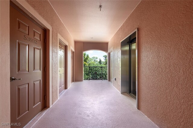 hall featuring a textured ceiling, elevator, and light colored carpet