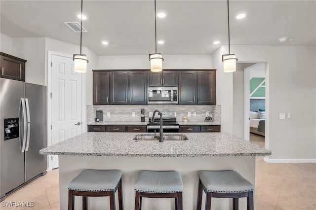 kitchen with hanging light fixtures, sink, appliances with stainless steel finishes, and an island with sink