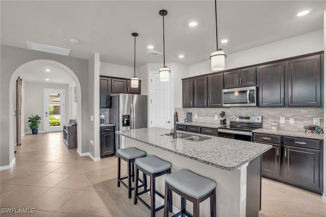 kitchen with a kitchen island with sink, light stone counters, sink, and stainless steel appliances