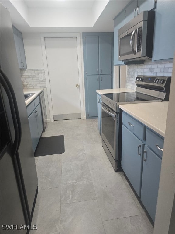 kitchen featuring appliances with stainless steel finishes, decorative backsplash, blue cabinets, and a tray ceiling