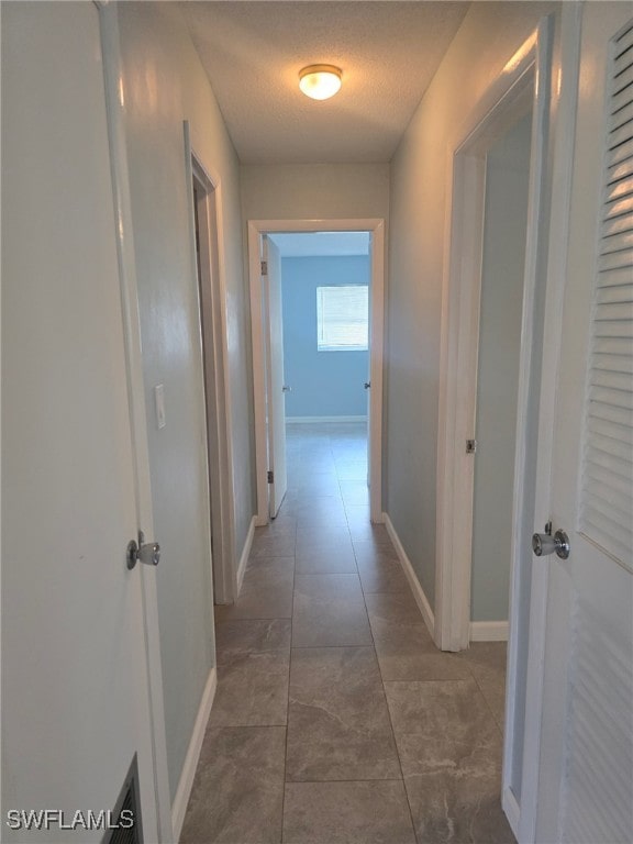 corridor featuring dark tile patterned flooring and a textured ceiling