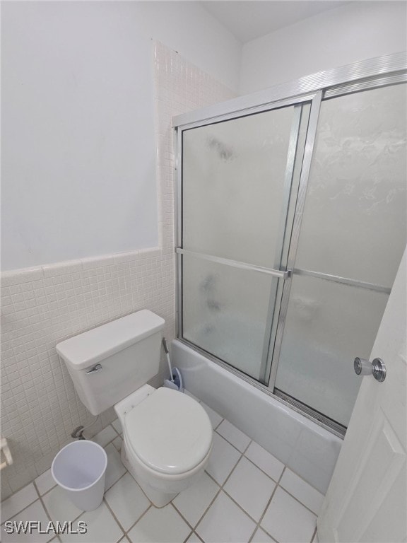 bathroom with tile walls, toilet, tile patterned floors, and combined bath / shower with glass door