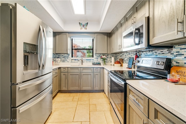 kitchen with tasteful backsplash, appliances with stainless steel finishes, sink, and a tray ceiling