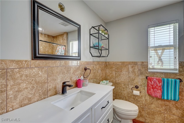 bathroom with tile walls, a wealth of natural light, vanity, and toilet