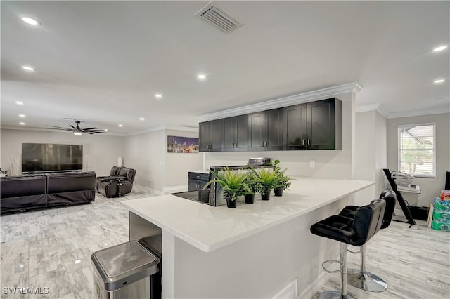 kitchen with ceiling fan, kitchen peninsula, a breakfast bar, crown molding, and light hardwood / wood-style floors