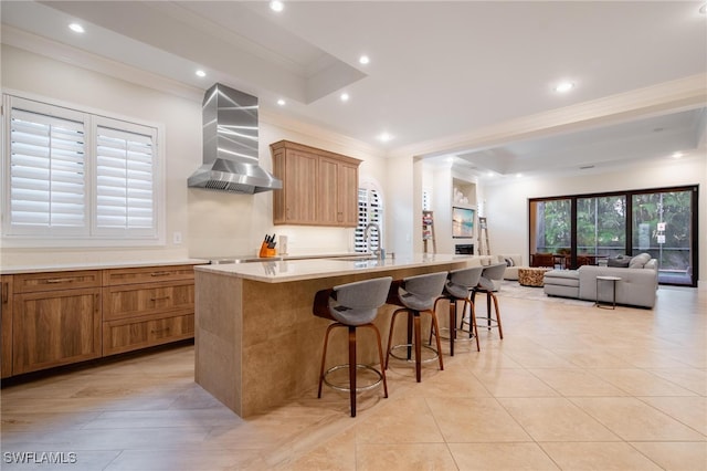 kitchen with sink, a spacious island, a kitchen breakfast bar, wall chimney exhaust hood, and crown molding