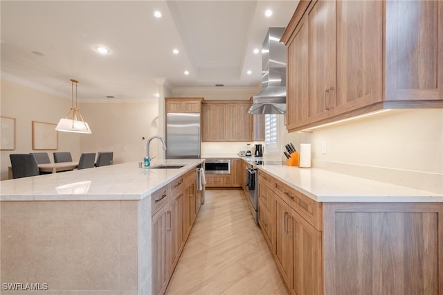 kitchen featuring wall chimney range hood, hanging light fixtures, a spacious island, stainless steel appliances, and sink