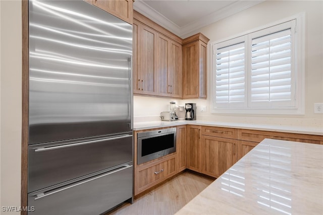 kitchen with ornamental molding, appliances with stainless steel finishes, and light hardwood / wood-style flooring