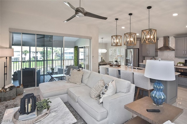 living room with ceiling fan with notable chandelier, sink, light hardwood / wood-style flooring, and plenty of natural light