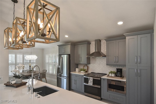 kitchen featuring decorative light fixtures, an inviting chandelier, appliances with stainless steel finishes, and wall chimney range hood