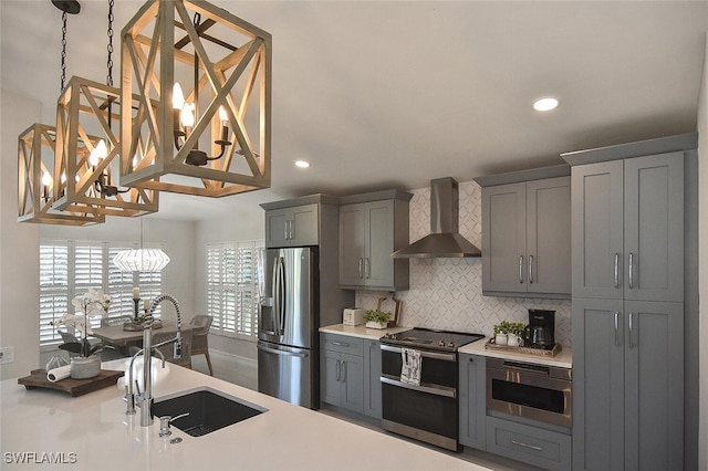 kitchen with decorative backsplash, a sink, stainless steel appliances, wall chimney exhaust hood, and gray cabinets