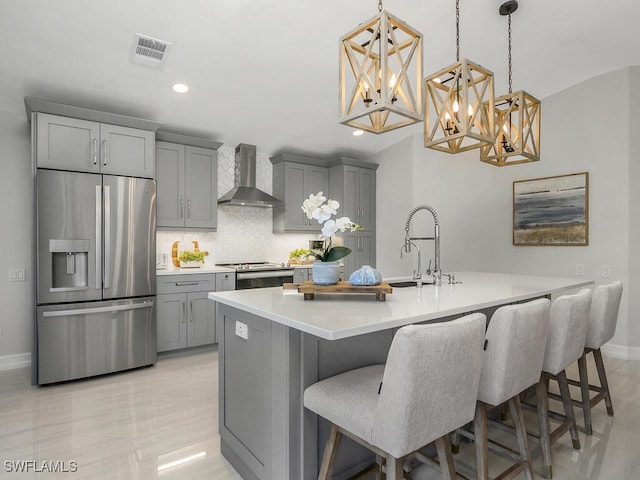 kitchen with pendant lighting, stainless steel appliances, wall chimney range hood, and a breakfast bar