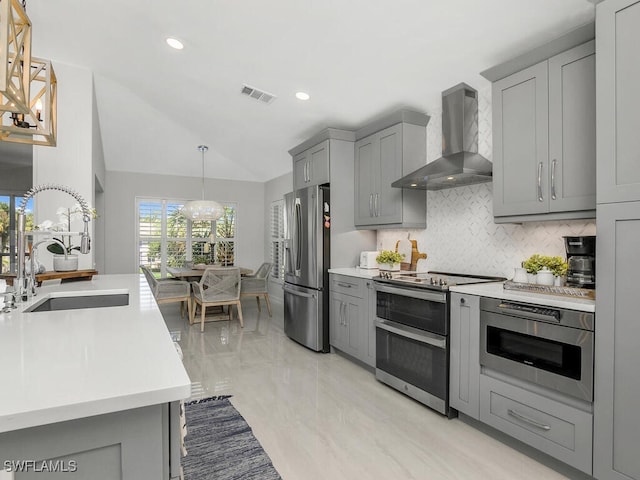 kitchen featuring a chandelier, pendant lighting, gray cabinets, stainless steel appliances, and wall chimney range hood