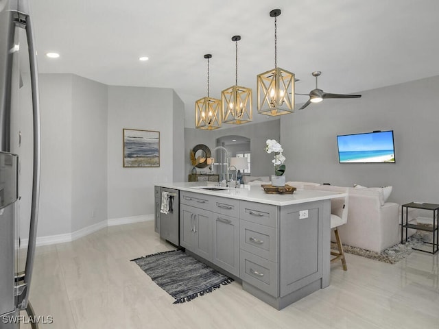 kitchen featuring ceiling fan, hanging light fixtures, a center island with sink, gray cabinets, and a breakfast bar