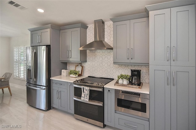 kitchen featuring gray cabinets, stainless steel appliances, light countertops, wall chimney range hood, and visible vents