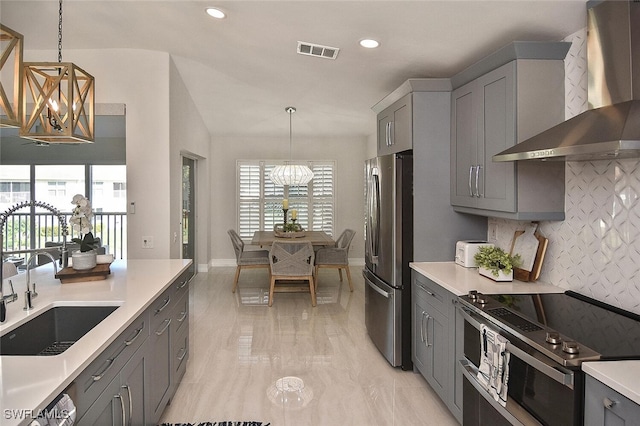 kitchen with wall chimney range hood, a sink, a chandelier, stainless steel appliances, and gray cabinets