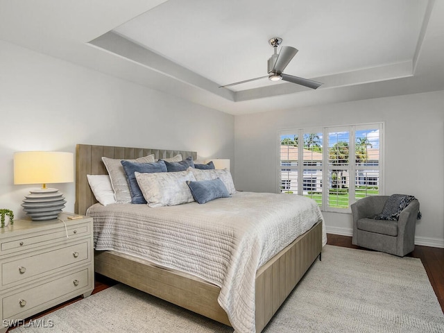 bedroom featuring baseboards, a ceiling fan, light wood-style flooring, and a tray ceiling