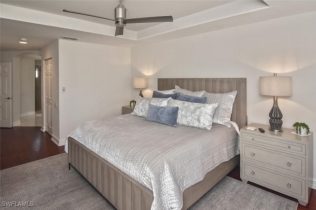 bedroom with wood finished floors, arched walkways, ceiling fan, baseboards, and visible vents
