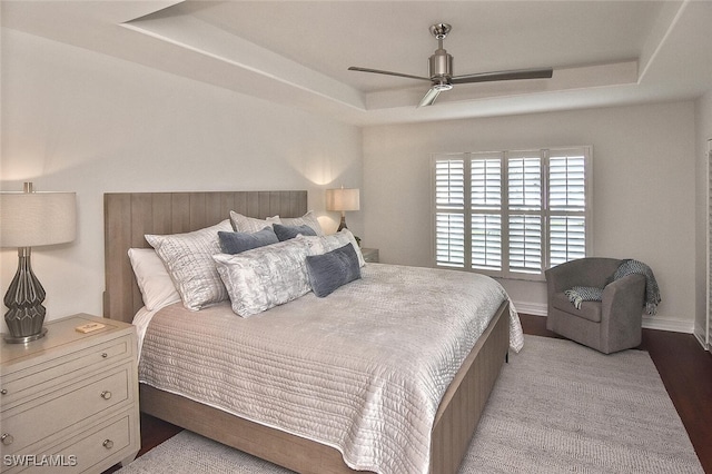 bedroom with ceiling fan, a tray ceiling, and light hardwood / wood-style flooring