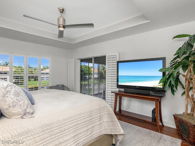 bedroom with ceiling fan, a raised ceiling, dark hardwood / wood-style flooring, and access to outside