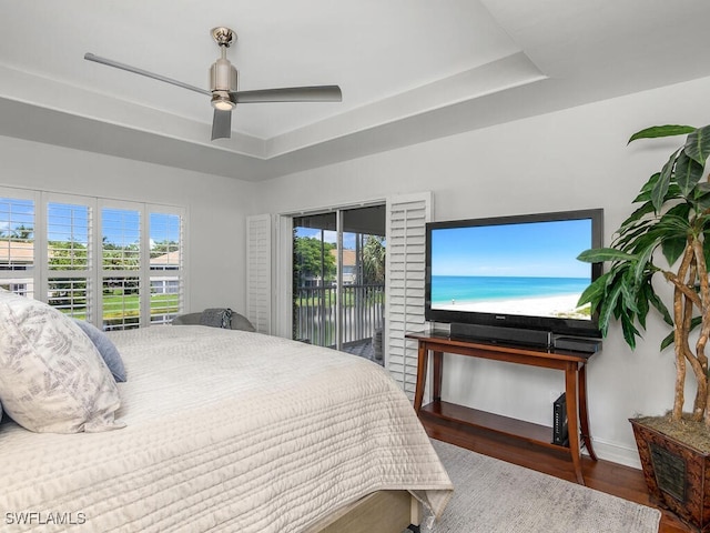 bedroom featuring wood finished floors, access to outside, ceiling fan, baseboards, and a tray ceiling