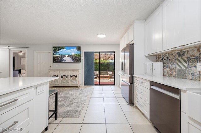 kitchen featuring white cabinetry, tasteful backsplash, a barn door, light tile patterned floors, and stainless steel appliances