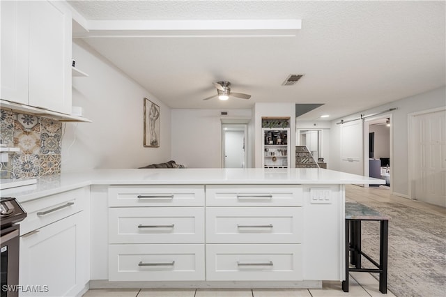 kitchen with ceiling fan, a barn door, kitchen peninsula, and white cabinetry