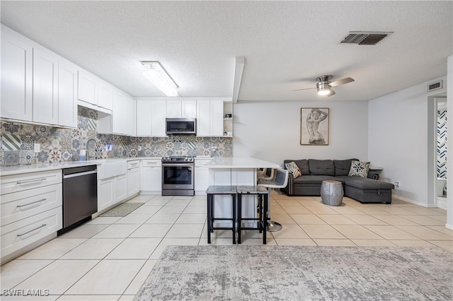 kitchen with stainless steel appliances, white cabinetry, ceiling fan, and a kitchen bar