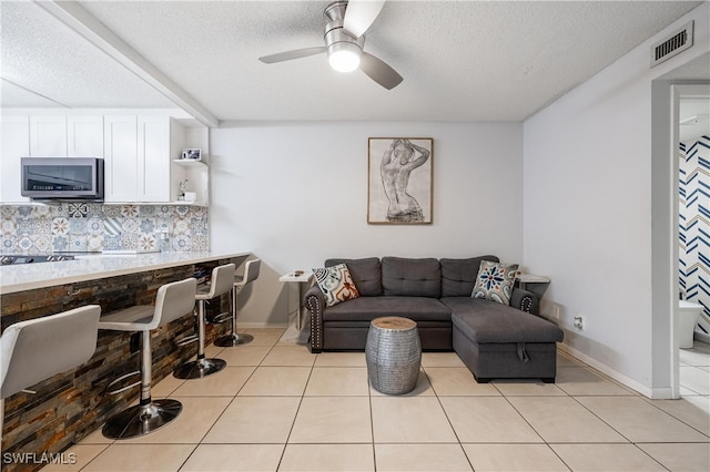 living room featuring a textured ceiling, light tile patterned floors, and ceiling fan