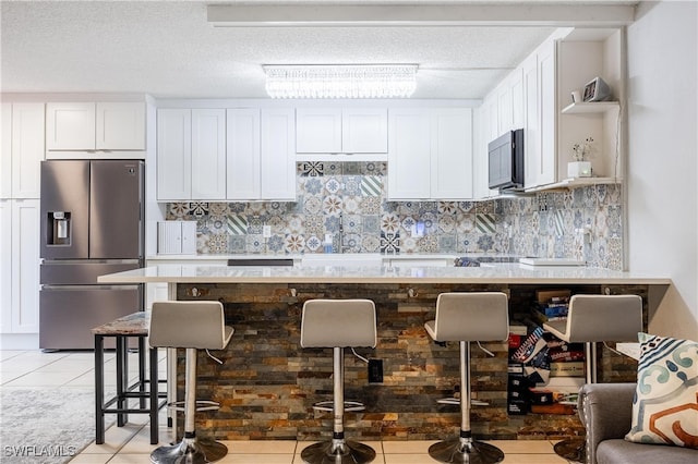 kitchen with a breakfast bar, stainless steel fridge with ice dispenser, tasteful backsplash, white cabinetry, and light tile patterned floors