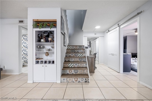 stairway featuring a textured ceiling, a barn door, and tile patterned floors