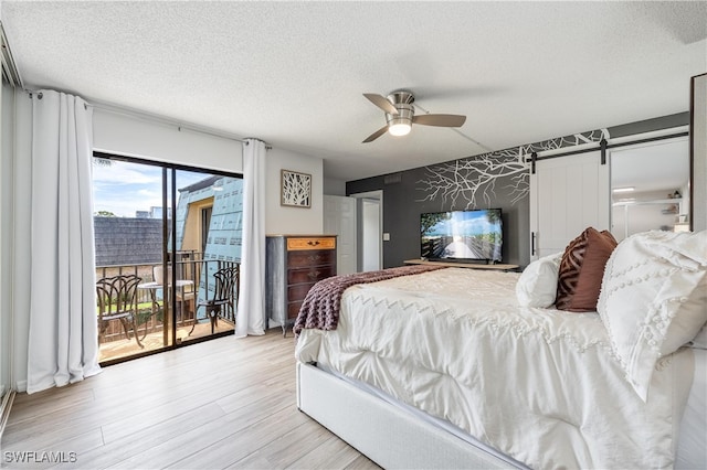 bedroom with a textured ceiling, light hardwood / wood-style floors, access to exterior, a barn door, and ceiling fan