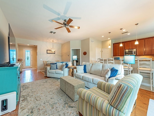 living room featuring ceiling fan with notable chandelier and light hardwood / wood-style flooring