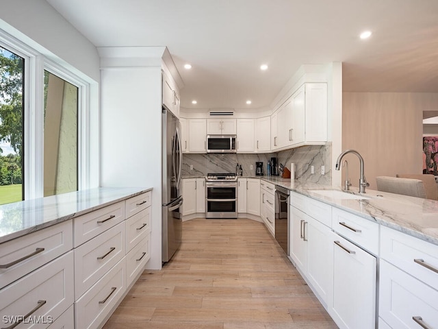 kitchen featuring light hardwood / wood-style floors, light stone counters, white cabinets, stainless steel appliances, and sink