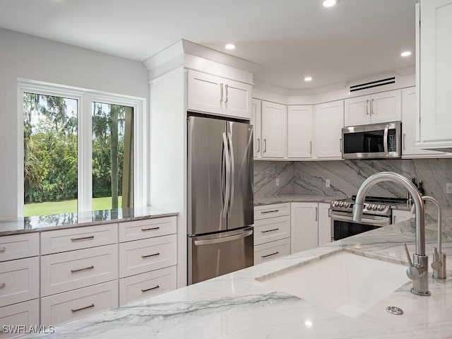 kitchen featuring white cabinets, backsplash, light stone countertops, stainless steel appliances, and sink