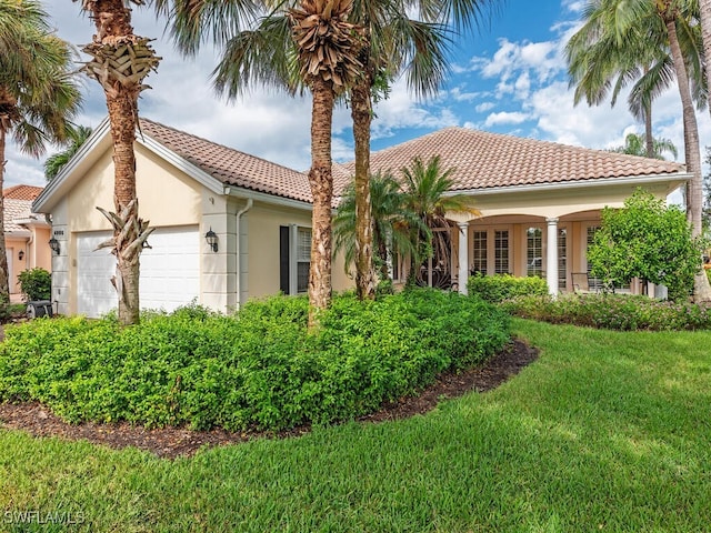 mediterranean / spanish house featuring an attached garage, a tiled roof, a front lawn, and stucco siding