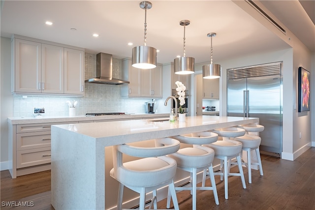 kitchen with pendant lighting, a center island with sink, wall chimney exhaust hood, dark hardwood / wood-style floors, and stainless steel appliances