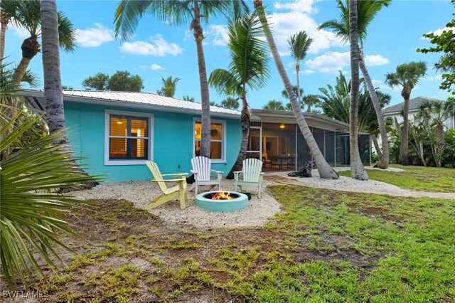 rear view of house with a patio, a lawn, a sunroom, and a fire pit