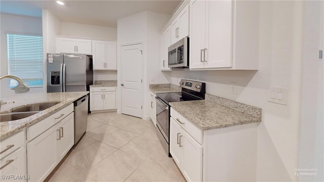 kitchen with light stone counters, stainless steel appliances, sink, light tile patterned floors, and white cabinets