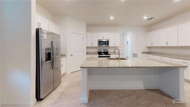 kitchen with light stone countertops, sink, stainless steel appliances, a kitchen island with sink, and white cabinets