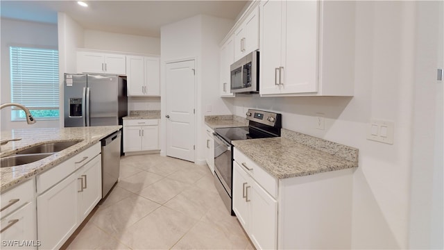 kitchen with light stone countertops, appliances with stainless steel finishes, sink, light tile patterned floors, and white cabinets